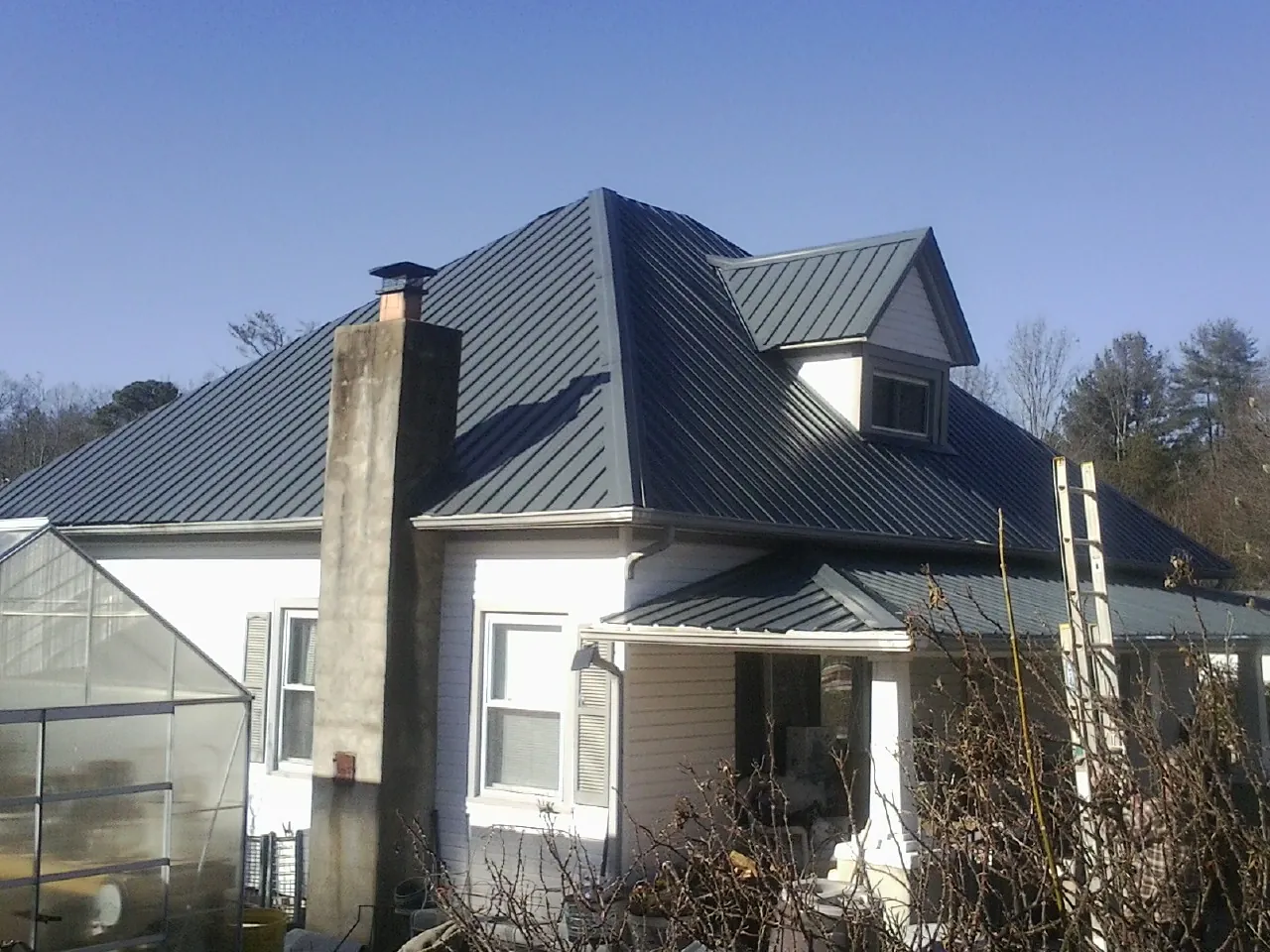 Dark blue standing seam metal roof on a white farmhouse with dormer — Slate & Tile Roof Repair by Roofing Brothers in Rotonda West