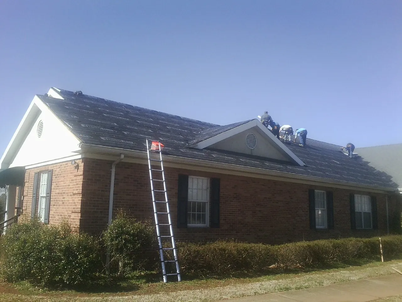 Crew tearing shingles off a brick ranch roof with a ladder set — Emergency Roof Repair work by our crew in Rotonda West