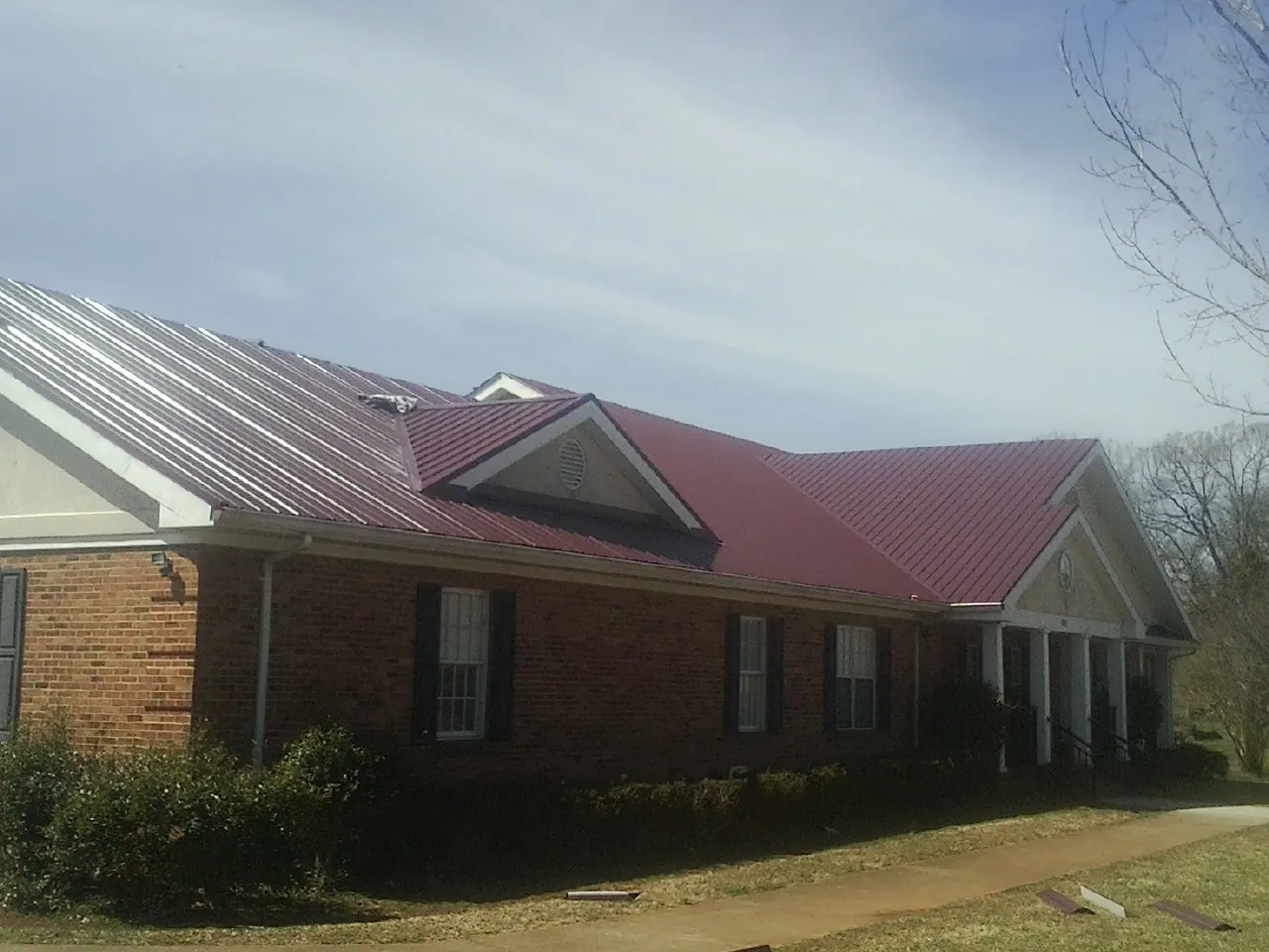 Red metal roof with gabled entries on a long brick building, from a Hail Damage Roof Repair job in Rotonda West