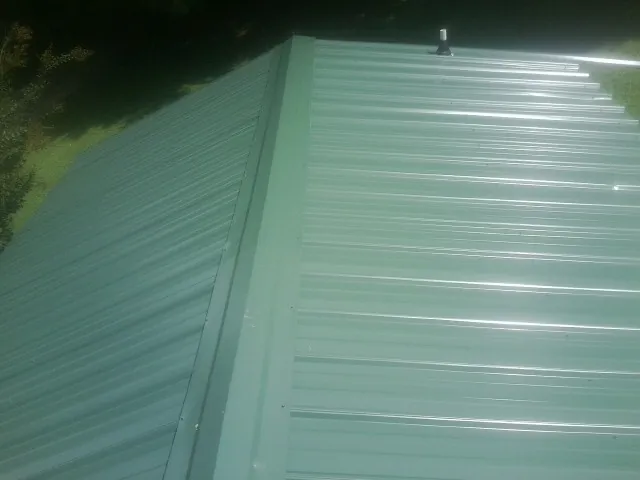 New green metal panels meeting at the ridge of a roof — Flat Roof Repair work by our crew in Rotonda West
