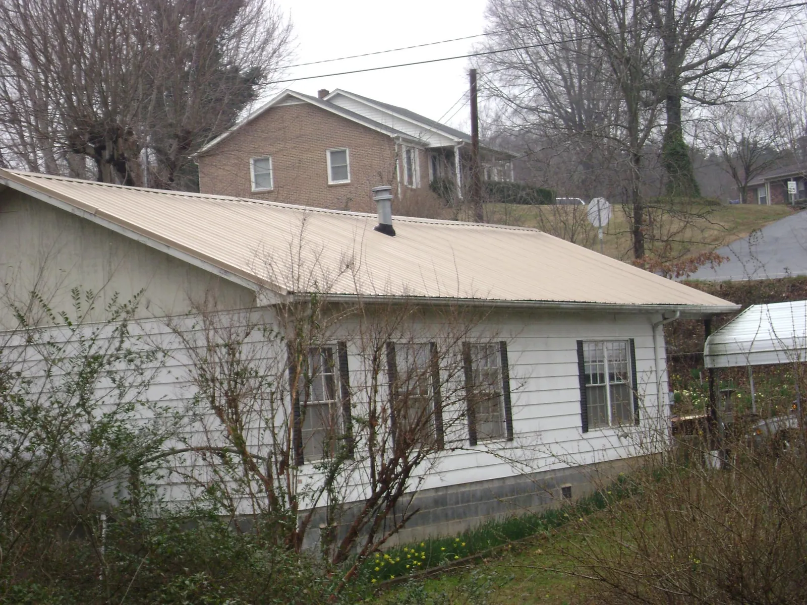 Tan metal roof on a white sided house set into a hillside — Commercial Roofing by Roofing Brothers in Rotonda West